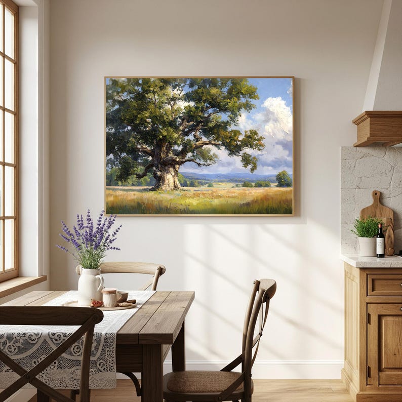 May include: A framed landscape painting shows a large oak tree in a field under a blue sky with white clouds. The tree's green leaves contrast with the golden field. The artwork hangs above a wooden table and chairs.