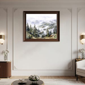 May include: A framed watercolor painting of a misty mountain landscape. The artwork depicts evergreen trees and rolling hills shrouded in fog. The frame is a dark brown color, and the painting is displayed on a white wall.