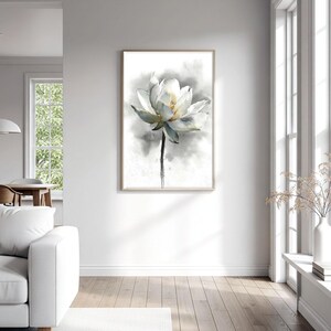 May include: A framed watercolor painting of a white lotus flower with a yellow center and green-blue tinged petals. The flower is set against a soft, gray background. The artwork is displayed in a bright, modern living room.