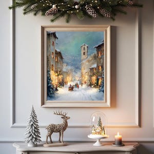 Puede incluir: Una pintura enmarcada de una escena invernal con una calle nevada y edificios. Una figura decorativa de ciervo, un peque&ntilde;o &aacute;rbol de Navidad y una c&uacute;pula de cristal con un pueblo en miniatura est&aacute;n sobre una mesa. Una vela encendida y una guirnalda completan la escena.