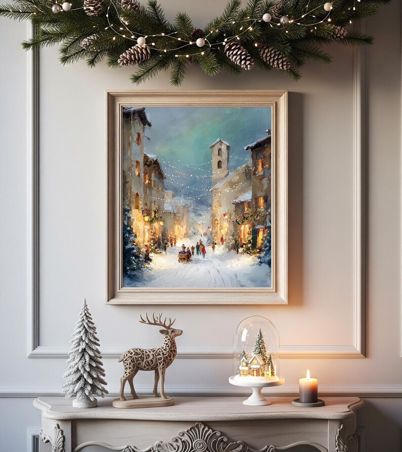Puede incluir: Una pintura enmarcada de una escena invernal con una calle nevada y edificios. Una figura decorativa de ciervo, un peque&ntilde;o &aacute;rbol de Navidad y una c&uacute;pula de cristal con un pueblo en miniatura est&aacute;n sobre una mesa. Una vela encendida y una guirnalda completan la escena.