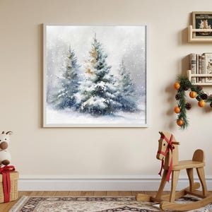 May include: A framed watercolor painting depicts a snowy winter scene with evergreen trees. The artwork features a soft, muted color palette of blues, whites, and touches of gold, evoking a serene, wintry atmosphere. The painting is displayed on a light-colored wall.