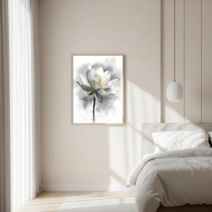 May include: A framed watercolor painting of a white lotus flower with a yellow center and blue-green accents. The flower is set against a soft gray background, creating a serene and elegant aesthetic. The artwork is displayed in a bedroom.