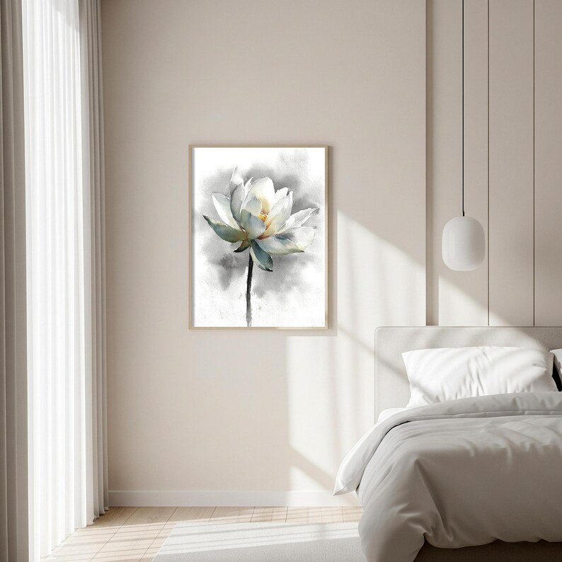 May include: A framed watercolor painting of a white lotus flower with a yellow center and blue-green accents. The flower is set against a soft gray background, creating a serene and elegant aesthetic. The artwork is displayed in a bedroom.