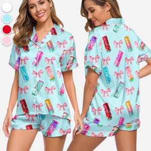 May include: Light blue pajama set with a pattern of colorful lip balm tubes and pink bows. The set includes a short-sleeved button-up shirt and matching shorts, both trimmed with white piping.