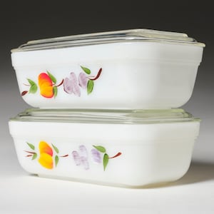 Puede incluir: Dos fuentes rectangulares blancas con tapas de vidrio apiladas. Cada fuente está decorada con un diseño floral pintado a mano con flores naranjas, amarillas y moradas con hojas verdes.