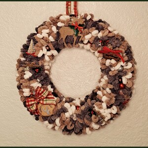 May include: A brown and white yarn wreath with various Christmas decorations, including a reindeer, a small tree, a bow, and a sign that says "Merry Christmas".