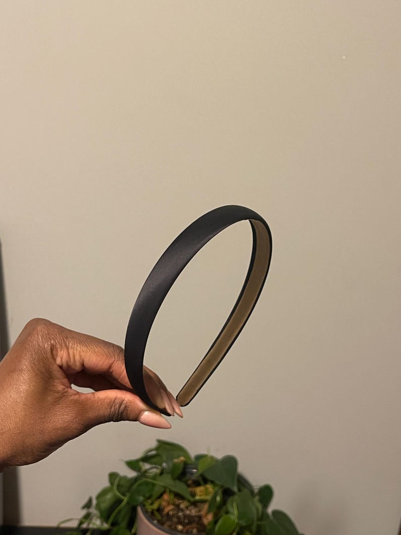 May include: A black satin headband. The headband is thin and has a simple design.