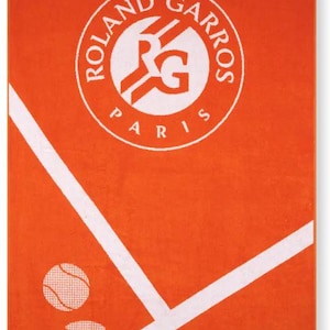 May include: Orange towel featuring the Roland-Garros logo and text. The towel design includes a tennis court graphic with a tennis ball. The text "ROLAND-GARROS 2025" is displayed at the top and bottom in white on a navy blue background.
