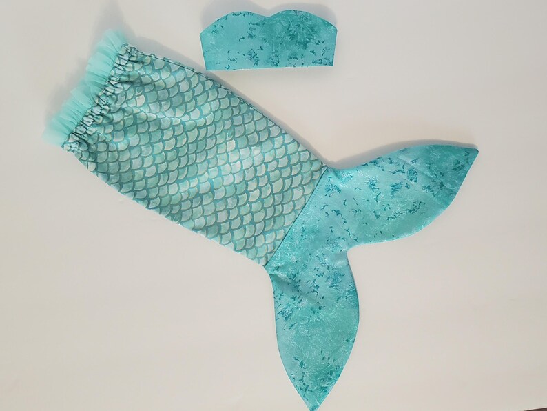 May include: A turquoise mermaid tail and matching top. The tail features a scale pattern on the upper portion and a solid, textured design on the fin. The top is a bandeau style, also in turquoise.