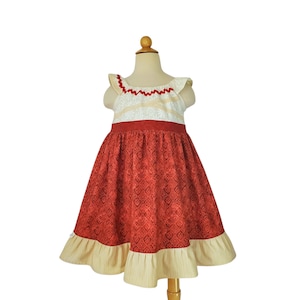 May include: A red patterned dress with a cream bodice and a red ribbon waist. The dress has a ruffled hem and is displayed on a mannequin. The dress is designed for children.