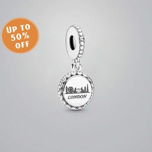 Puede incluir: Un charm de plata con temática de Londres. El charm presenta un colgante redondo con una silueta negra del London Eye, el Tower Bridge y otros monumentos. La palabra "LONDON" está impresa debajo. El charm tiene un borde decorativo y una fianza en forma de corazón.