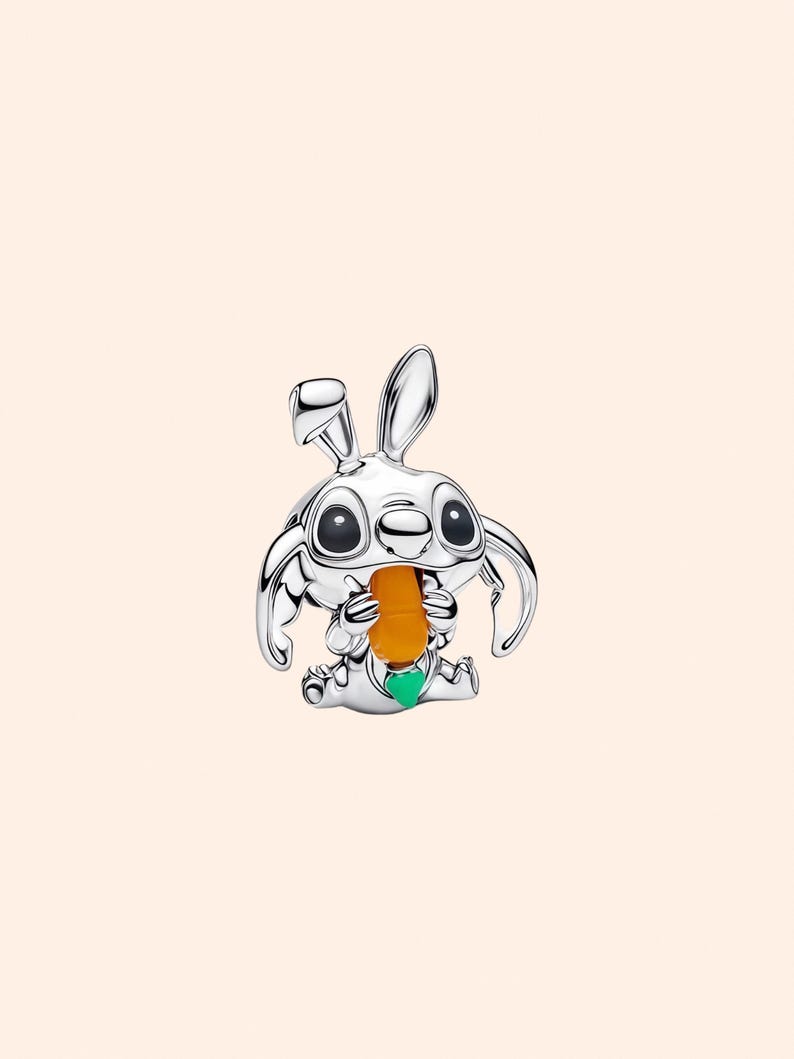 May include: A silver-colored charm depicting a cartoon rabbit holding a carrot. The rabbit has large eyes and long ears. The carrot is orange, and the charm has a green accent.