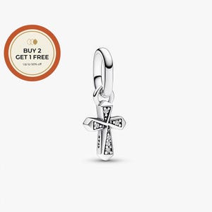 Puede incluir: Un charm de cruz plateada con un lazo para pulsera o collar. La cruz está adornada con pequeñas piedras preciosas transparentes y tiene un diseño detallado. El charm está suspendido sobre un fondo blanco.