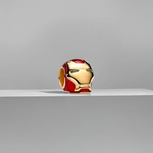 Könnte beinhalten: Ein gold-roter Iron Man Helm-Charm. Der Charm zeigt ein detailliertes Design des ikonischen Helms des Superhelden, mit goldenen Akzenten und roter Emaille. Der Charm ist ein Sammlerstück, perfekt für Fans der Marvel-Comics und -Filme.
