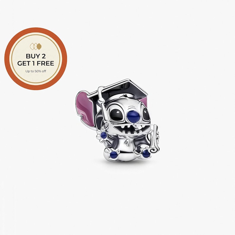 May include: A silver charm featuring a cartoon character wearing a graduation cap and holding a diploma. The character has large black eyes, blue accents, and pink ears. The charm is detailed and sits on a white background.