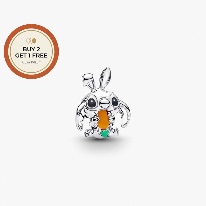 May include: A silver-colored charm in the shape of a cartoon character with large eyes and rabbit-like ears, holding an orange carrot. The charm has a green accent and is set against a white background. The image also includes a circular graphic with text that reads "BUY 2 GET 1 FREE Up to 50% off."