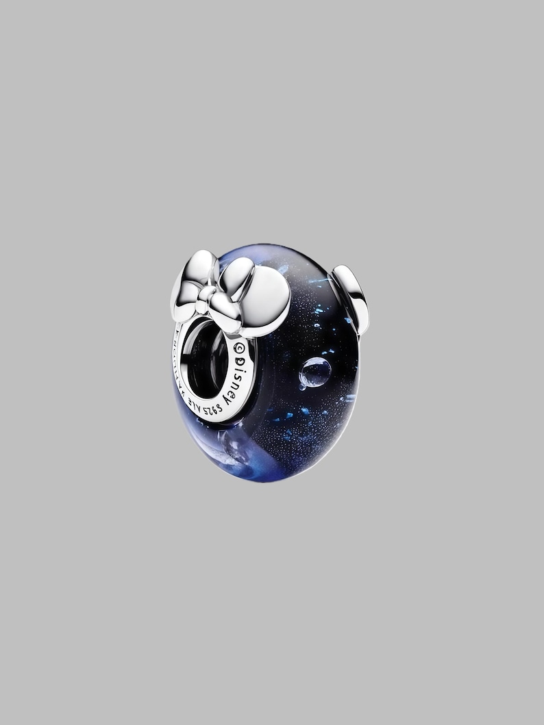 Pode incluir: Um berloque de prata com um n&uacute;cleo azul escuro e preto, com um la&ccedil;o e dois detalhes circulares. O berloque tem as palavras "Disney" e "S925 ALE" gravadas.