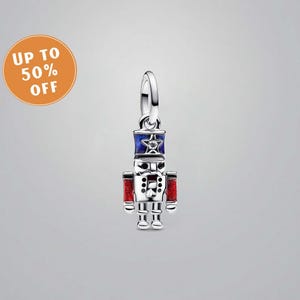 Pode incluir: Um berloque prateado em forma de quebra-nozes. O berloque apresenta um design pintado em azul e vermelho, com uma estrela no chapéu. Possui uma argola para prender a uma pulseira ou colar. Um item festivo, ideal para uma pulseira de berloques.