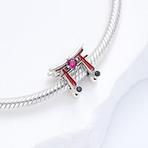 K&ouml;nnte beinhalten: Ein silberner Charm mit einem roten und silbernen Torii-Tor-Design, verziert mit einem rosa Edelstein und schwarzen Details. Der Charm ist an einem silbernen Armband befestigt, mit japanischem Thema.