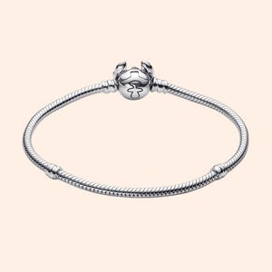 Puede incluir: Una pulsera plateada con un dije redondo con un dise&ntilde;o estilizado. La pulsera tiene un dise&ntilde;o de cadena de serpiente y un cierre de broche. El dije tiene un patr&oacute;n detallado y est&aacute; centrado en la pulsera.