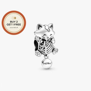 Può includere: Un charm d'argento a forma di gatto che tiene in mano un gomitolo di lana. Il charm ha un ciondolo rotondo pendente con la scritta "MEOW" incisa. Il charm a forma di gatto è dettagliato con impronte di zampe e tratti del viso.