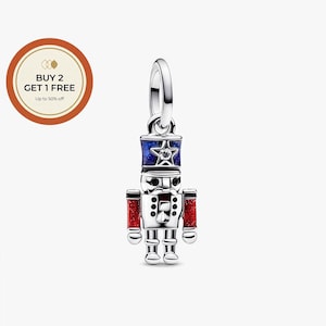 May include: A silver-colored charm in the shape of a toy soldier nutcracker. The nutcracker has a blue and red hat, red arms, and a star-shaped gem. The charm has a loop at the top for attaching to a bracelet or necklace.