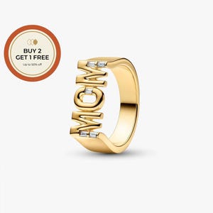 Peut inclure: Une bague dorée avec le mot "MOM" épelé en majuscules. La bague comporte de petites pierres précieuses claires et rectangulaires incrustées dans les lettres. Un graphique circulaire avec le texte "BUY 2 GET 1 FREE" est dans le coin supérieur gauche.