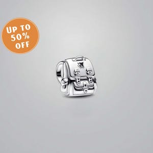 Puede incluir: Un charm de mochila plateada con cierres, bolsillos y un asa superior detallados. El charm tiene un pequeño diseño de avión. Un círculo naranja con el texto "UP TO 50% OFF" está en la esquina superior izquierda.