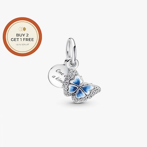 May include: A silver butterfly charm with blue enamel wings and clear crystal accents. A small, round charm with the words "One of a kind" is attached. The charm is designed to be worn as a pendant or bracelet charm.