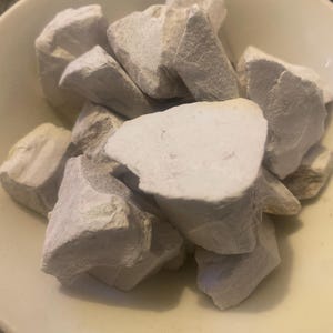 May include: A light yellow bowl is filled with a collection of off-white, irregularly shaped rocks. The rocks have a rough, textured surface and vary in size. The bowl's rim is visible, creating a simple, natural composition.