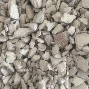 May include: A close-up of a collection of pale grey, irregularly shaped stones. The stones are of varying sizes and textures, some smooth and others rough. The overall colour is a muted, neutral tone, with slight variations in shade.