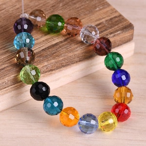 May include: A strand of faceted glass beads in various colors, including purple, blue, green, brown, yellow, orange, and red. The beads are strung on a clear thread and are arranged in a rainbow pattern.