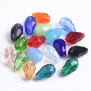Op de afbeelding: Assortiment van kleurrijke glazen druppelvormige kralen in verschillende tinten blauw, groen, rood, roze en helder. De kralen zijn gefacetteerd en hebben een parelmoer afwerking.