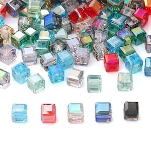 May include: A selection of multi-coloured, faceted glass beads in shades of blue, green, red, and clear. The cube-shaped beads are made of crystal or glass, reflecting light. Suitable for jewellery making and crafts.