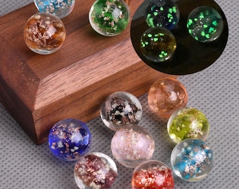 May include: A collection of clear glass marbles with colorful inclusions. The marbles feature various colors, including blue, green, brown, and red, with shimmering accents. Some marbles glow in the dark, showcasing a unique design.