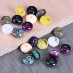 May include: Assortment of colorful round beads with various patterns and colors, including purple, blue, yellow, white, and brown. The beads are made of different materials, such as glass, plastic, and wood.