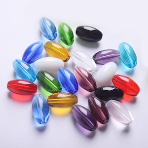 Puede incluir: Surtido de cuentas de vidrio ovaladas en varios colores, incluyendo rojo, azul, verde, amarillo, morado, negro y transparente.