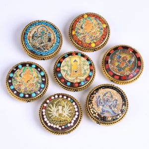 May include: Seven round, gold-toned, decorative pendants with colorful, intricate designs featuring various Buddhist deities. Each pendant is surrounded by a beaded border.