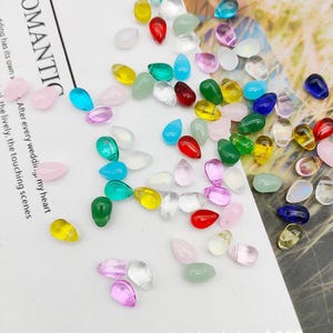 May include: Assortment of colourful teardrop shaped glass beads. The beads are in various colours including pink, blue, green, yellow, red, and clear.