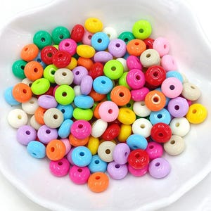 May include: A large assortment of colorful plastic donut beads. The beads are in various shades of pink, blue, green, yellow, orange, and red.