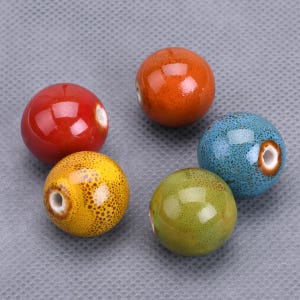 Könnte beinhalten: Fünf Keramikperlen in verschiedenen Farben: Rot, Gelb, Grün, Blau und Orange. Die Perlen sind rund und haben eine glatte, glänzende Oberfläche. Sie eignen sich perfekt für die Schmuckherstellung oder andere Bastelarbeiten.