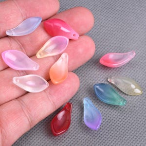 Könnte beinhalten: Sortiment an bunten, durchsichtigen, tropfenförmigen Perlen mit einem Loch oben zum Aufziehen. Die Perlen sind in verschiedenen Farbtönen von Rosa, Blau, Grün, Orange und Rot.