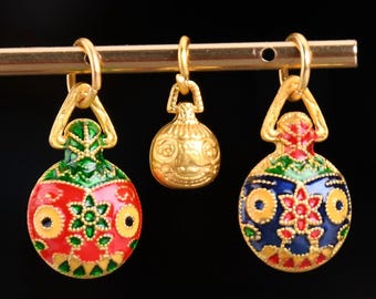 May include: Three gold charms with colorful enamel designs. The charms are round and have a loop at the top for hanging. One charm is red, green, and yellow with a flower design. Another charm is blue, green, and yellow with a flower design. The third charm is gold and has a detailed design.