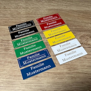 Könnte beinhalten: Zehn rechteckige Namensschilder mit dem Text "Familie Mustermann" in weißer Schrift auf verschiedenen farbigen Hintergründen, darunter Rot, Gelb, Grün, Blau und Weiß.