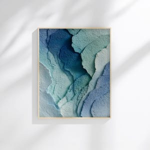 May include: Abstract wall art print featuring a textured design in shades of blue and teal. The artwork is framed in a light wood frame, creating a modern and serene aesthetic. The layered design evokes a sense of depth and movement.