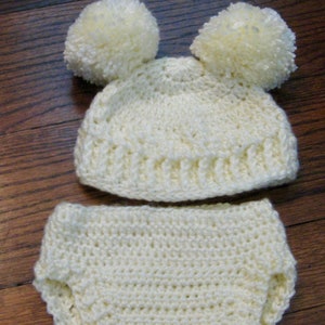 Puede incluir: Un gorro de bebé de ganchillo blanco con dos pompones esponjosos en la parte superior y un pañal de ganchillo blanco a juego.