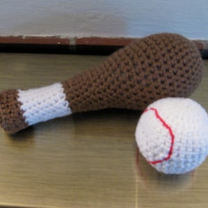 May include: A brown and white crocheted baseball bat and a white crocheted baseball with red stitching.
