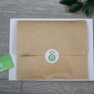 Op de afbeelding: Een bruin papieren pakket met een witte sticker waarop een groen logo staat van een bol garen met de letter "E" in het midden. De sticker is op een witte achtergrond.