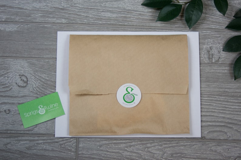 Op de afbeelding: Een bruin papieren pakket met een witte sticker waarop een groen logo staat van een bol garen met de letter "E" in het midden. De sticker is op een witte achtergrond.